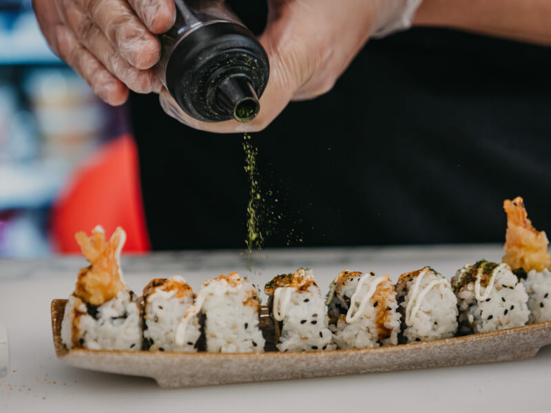 Some sprinkles green powder over handmade sushi rolls.